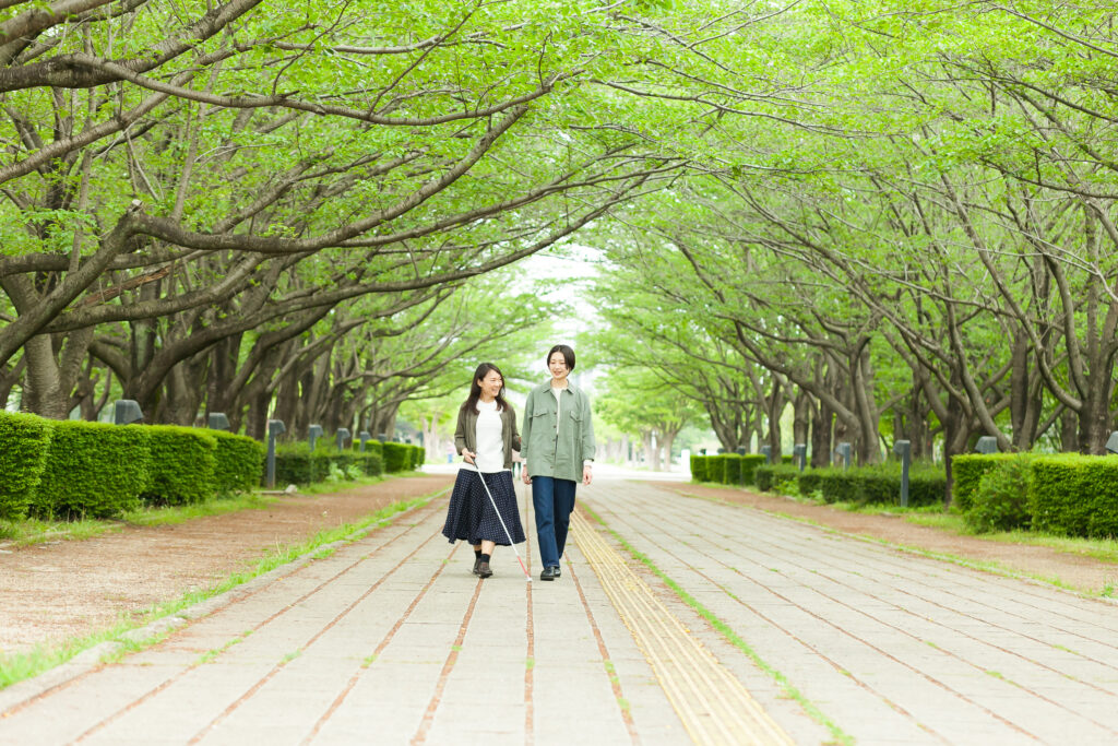 視覚障害者とガイドヘルパーの女性二人が公園の真ん中を歩いてきている画像。